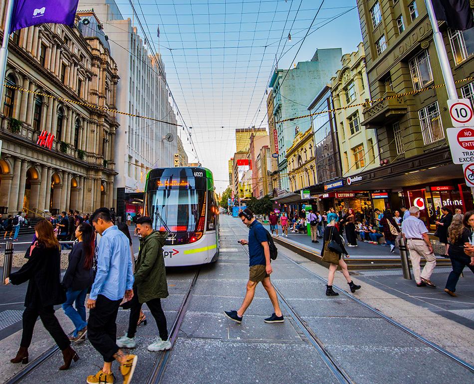 Crowds and trams on Bourke Street Mall at dusk.