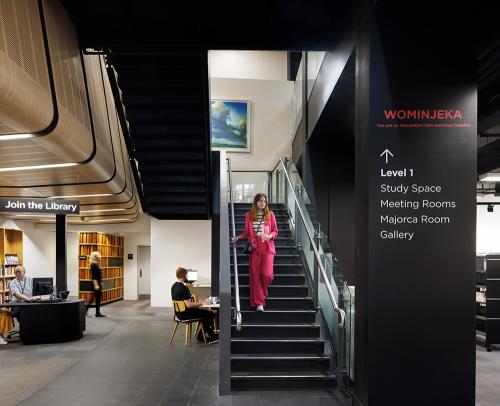 A stairway in a library with signs to study spaces, gallery and meeting rooms on level 1