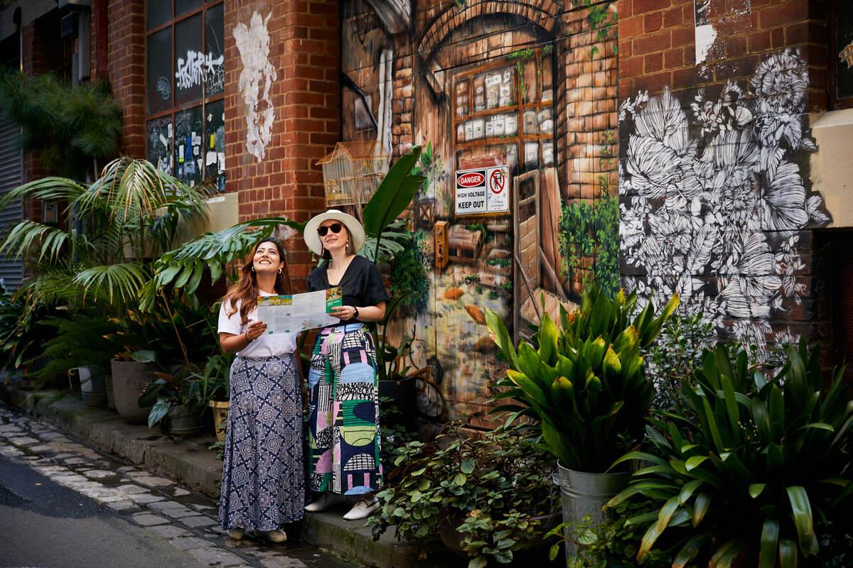 Two people in a laneway with graffiti and plants