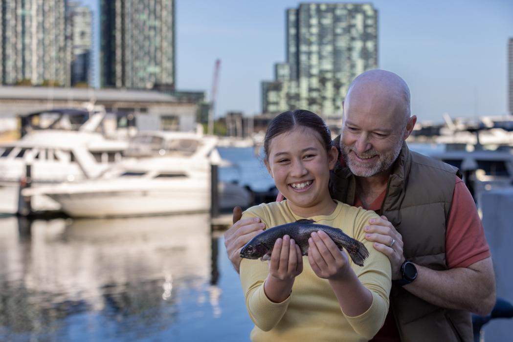 Girl holding up fish with proud father behind her at marina