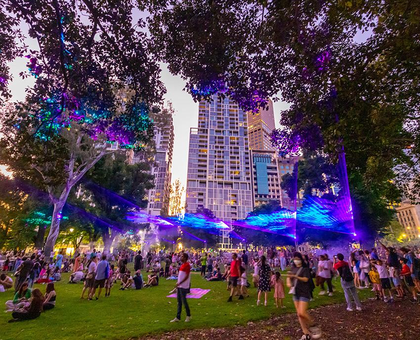 Crowds at an event in a park with blue radiating light installations.