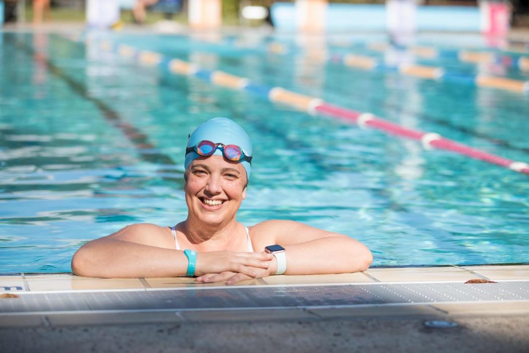 Female swimmer with arms on public pool edge smiling