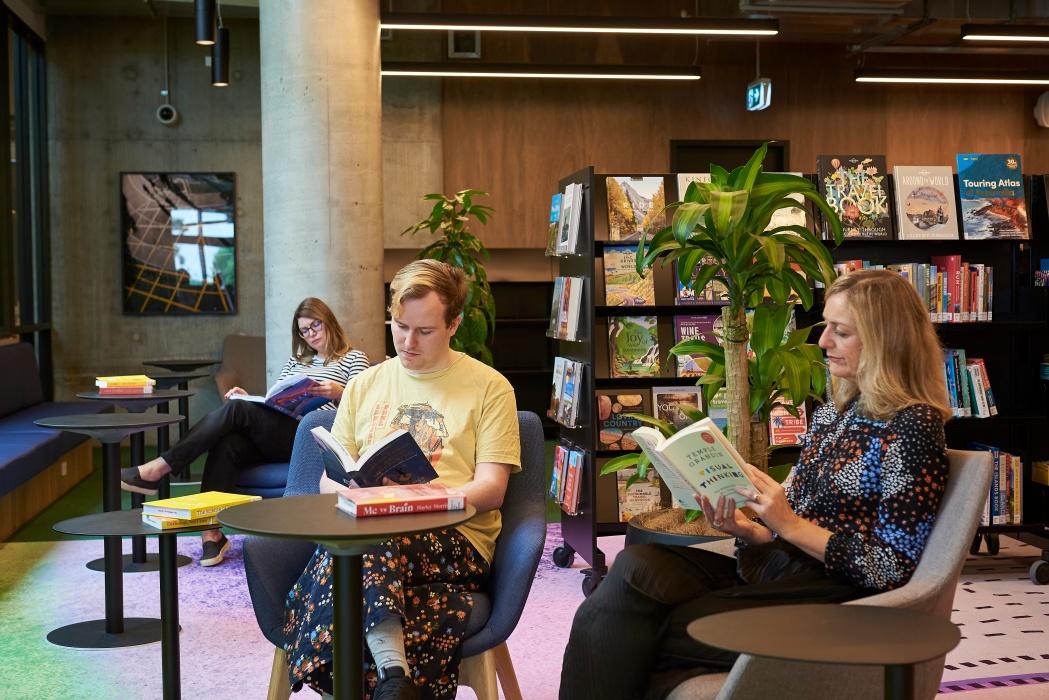 Three people sitting at tables reading books at library