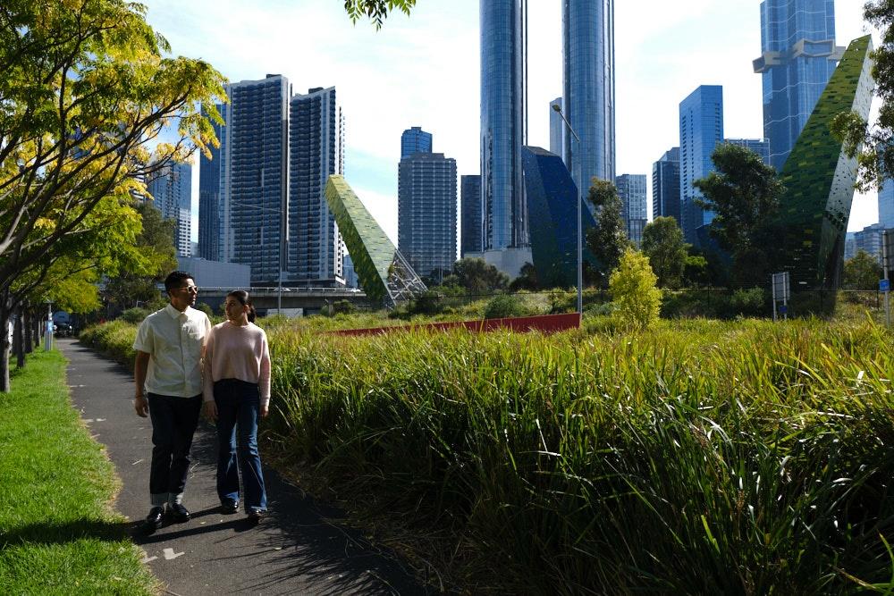 People walking next to greenery with city skyline in the background