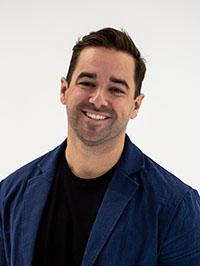 Smiling man with dark hair in blue suit jacket over black shirt