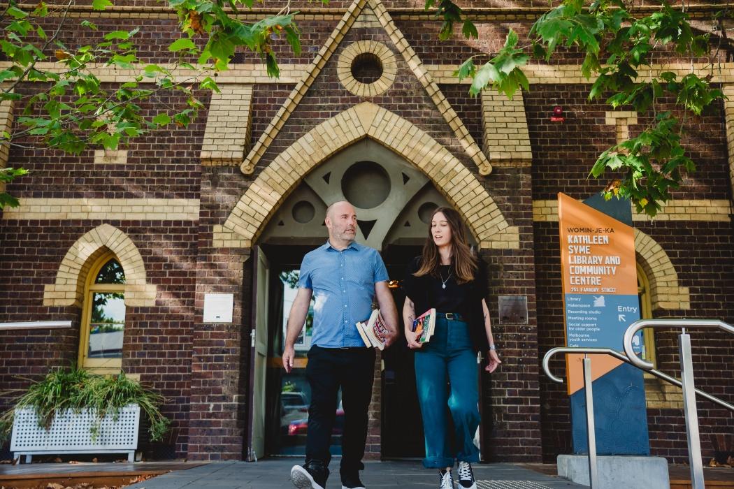 Man and woman coming out of Kathleen Syme Library holding books