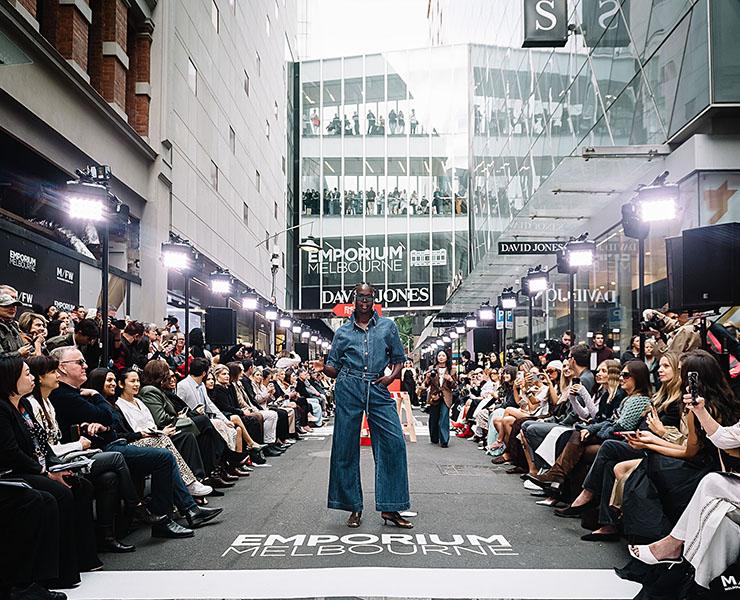Model stands and poses in the middle of the runway during Melbourne Fashion Week at Melbourne Emporium, while spectators watch from the sides.