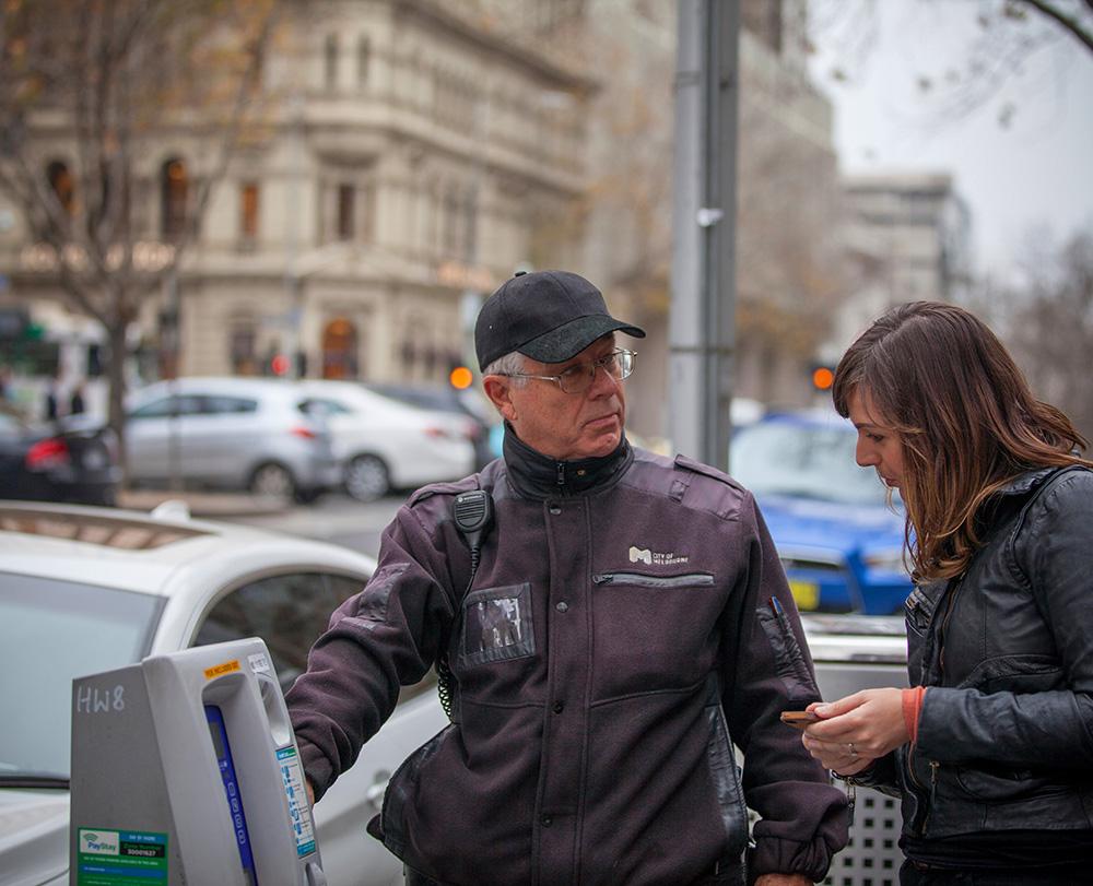 A parking officer helping a person with a ticket machine.