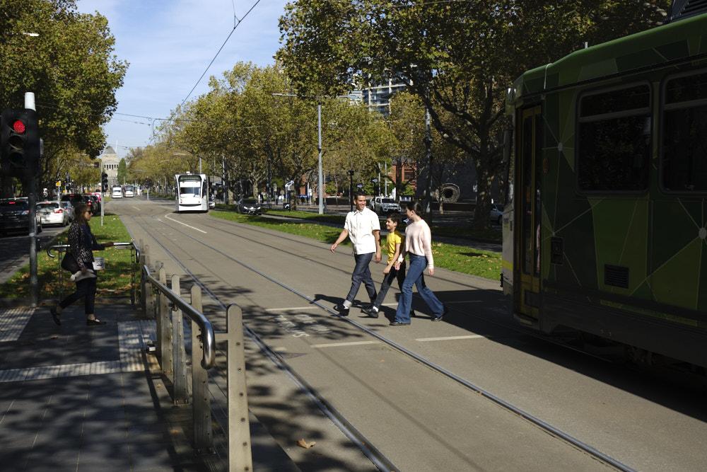 Two adults and a child crossing a road near a tram stop.