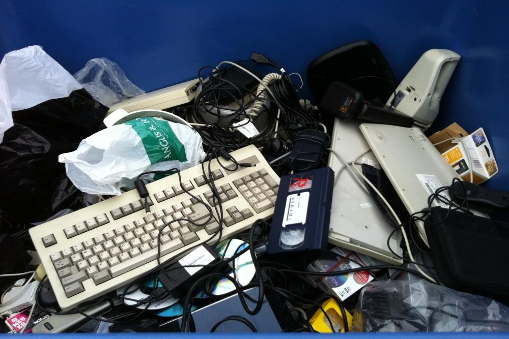 A pile of electronic waste including a computer keyboard, speakers and a VHS tape