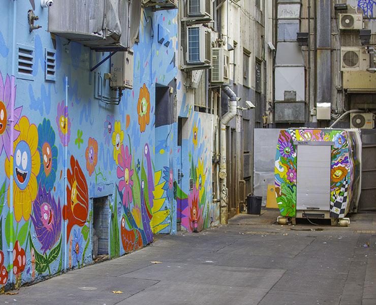 City laneway with colourful wall art of flowers, with recycling compactor in background.